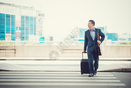 男人带着一个手提箱穿过公路离开机场图片