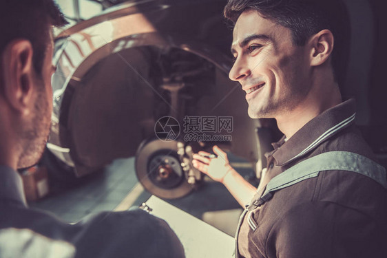 穿着制服的英俊年轻汽车机械师正在与客户交谈图片