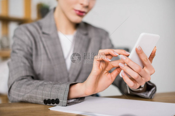 坐在办公室工作场所时使用智能手机的女商人被拍图片