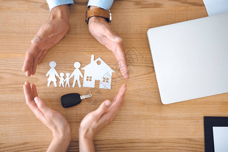 保险代理人和女手与房屋家庭纸张模型和木桌板上的钥图片