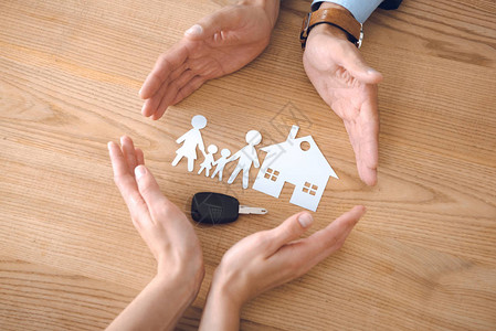 保险代理人和女手与房屋家庭纸张模型和木桌板上的钥图片