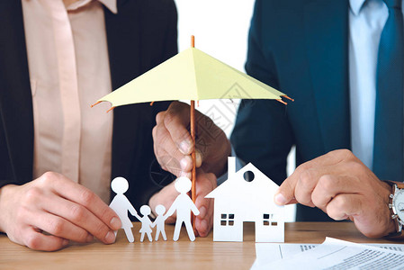 保险代理业者在工作场所以伞式保护覆盖家庭和住房纸张模型的部分观点图片