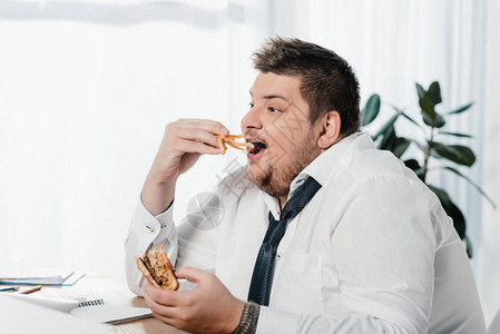 超重量体重商人在工作场所吃汉堡图片