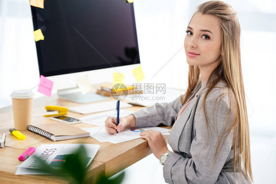 女营销经理在办公室工作场所做文书工作时看着图片