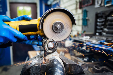一名年轻的焊工在车间里戴蓝色手套磨床金属角磨机背景图片