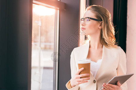 戴眼镜站立并持有数字平板电脑和咖啡杯图片