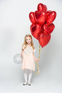 小姑娘拿着一捆红心形气球孤立在白背景图片