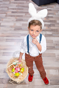小兔子耳朵里的小男孩拿着一篮子的复活节彩色鸡蛋背景图片