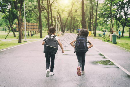 两个小学生跑去上学两个背着包的女孩秋天温暖的一天回到学校一图片