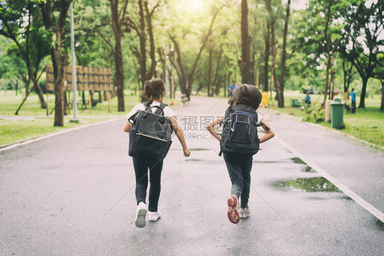 两个小学生跑去上学两个背着包的女孩秋天温暖的一天回到学校一图片
