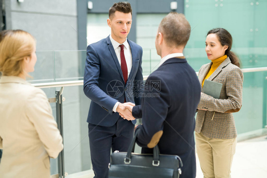英俊年轻商人在现代办公楼大厅与一群同事就利益交易后与合作伙图片