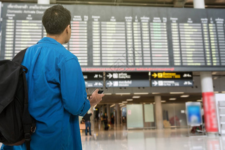 亚洲旅客手持智能手机在现代机场看航图片