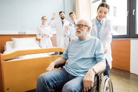 一群年轻的专业医生看着坐在轮椅上微笑的老年病人图片