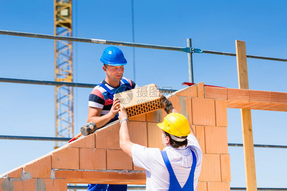 两名瓦工或建筑工人或工人在建筑或建筑工地上建造或砌砖或铺图片