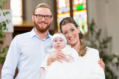在教堂的年轻父母带着婴儿穿图片