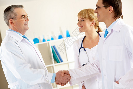 照片中年长的医生和年轻临床医生在与附近的美护士握手时图片