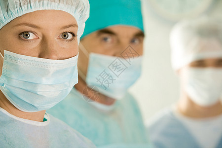 在同事的背景上佩戴保护面罩的外科女图片