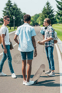 拥有书本和滑板的多族裔多族裔少年男孩站立背景图片