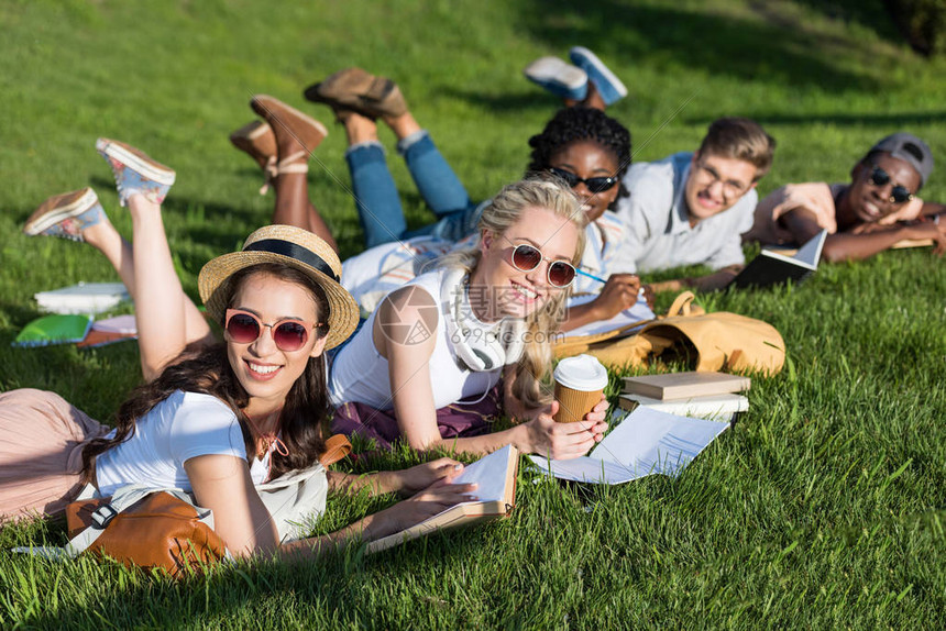 年轻多民族学生在公园中躺在绿草地上看书图片
