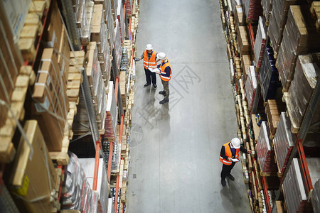 仓库工人组在一排装满包装箱和货物的高架之间的图片