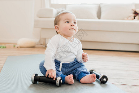 婴儿男孩坐在瑜伽垫子上和哑铃坐在图片