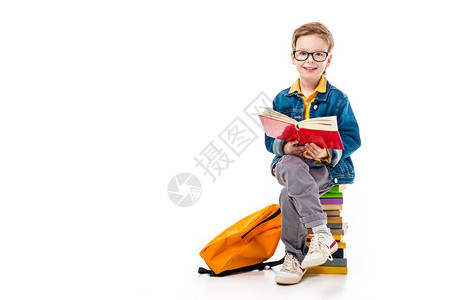 快乐的男孩阅读书坐在一堆书上背着包背景图片