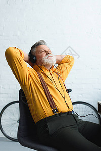 戴着耳机留着胡子的老人笑着坐在家里听音乐图片