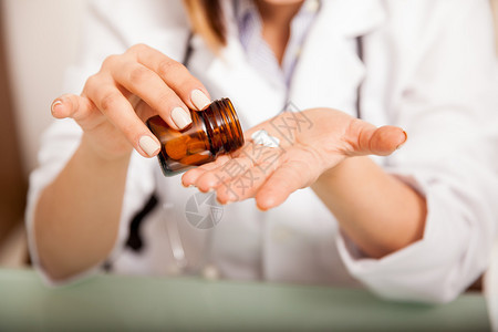 关闭女医生从瓶子上倒一些药的衣物图片