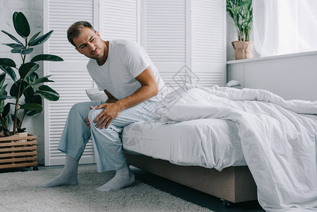 穿着睡衣的青年男子坐在床上在家中膝疼图片