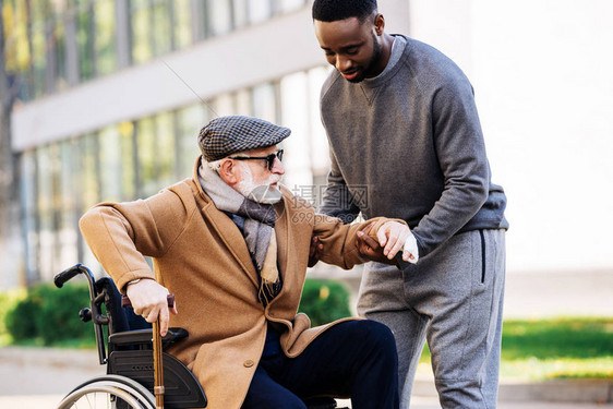 帮助老年残疾人在街上从轮椅上起身的非洲图片