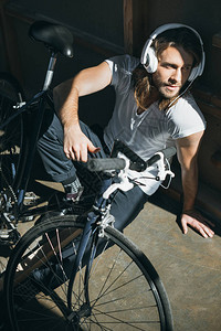 坐在自行车旁边和耳机监听音乐的英俊青年男子的高图片