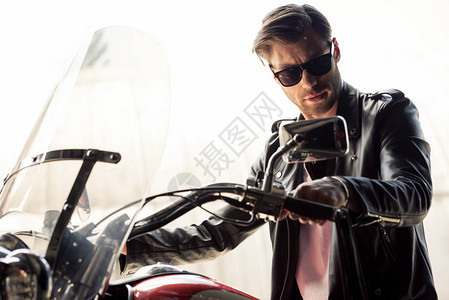 穿着太阳眼镜和皮夹克的帅气英俊年轻男子坐在摩托车上图片