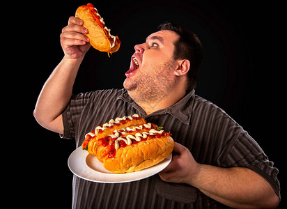 胖子在盘子上吃快餐热狗的饮食失败为贪吃很多的超重者提供早餐垃圾餐会导致肥胖被大量图片
