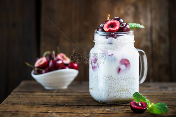 在深木背景的玻璃罐中用酸奶和樱桃从杏仁牛奶中的Chia种子出产的花层图片