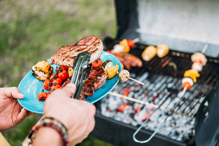 在公园的bbq时将烤食物放在盘子上背景图片