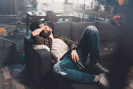 酒后在沙发上躺在沙发上喝着瓶子的醉胡须大图片素材