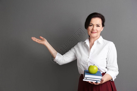 灰色背景中带笔记本和苹果的女教师肖像图片