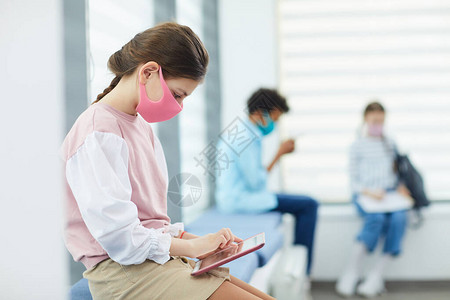 身着粉色面罩坐在学校医疗室和复印空间的Quque中背景图片