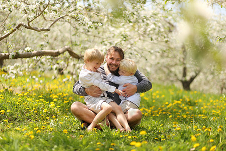 一个快乐的年轻父亲在春天的一天在白色开花的树下与他的两个年幼的孩子一起搔痒图片