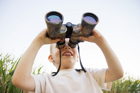 通过双筒望远镜在河岸上看的小男孩的画像可爱的孩子用双筒望远镜男孩通过双筒望图片