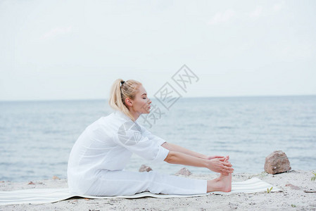 坐在海边瑜伽垫子上时有吸引力的妇图片