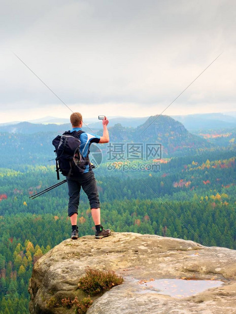 姜头发人在秋季山谷上方的岩石山峰上用智能手机拍照图片