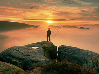 人独自站在岩石的顶端徒步旅行者在地平线上观看秋天的太阳美丽的时刻图片