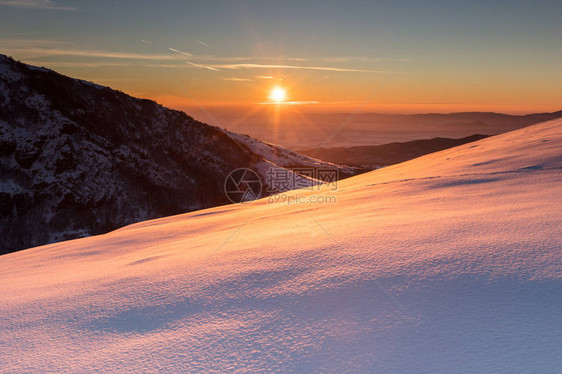 冬天的日出在红光中照亮了雪脊图片