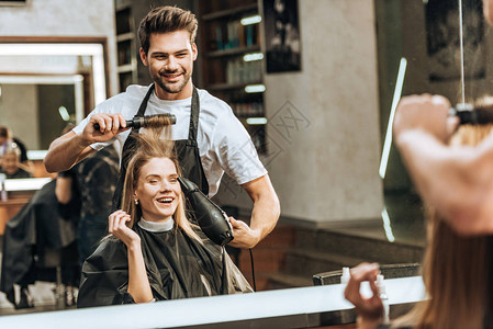 微笑着的年轻发型主义者梳理和烘干头发给美容院中快图片