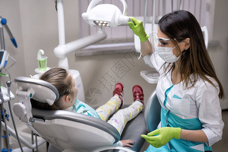 在牙科诊所为治疗准备灯光的牙医妇女她有小女图片