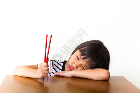 无聊的小女孩坐在桌边拿着红筷子图片