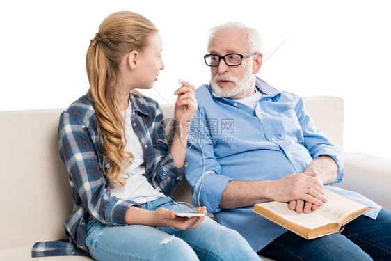 有书的祖父和有智能手机的孙子坐在沙发图片