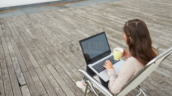 坐在椅子上膝上用笔记本电脑跪在膝上的妇女图片