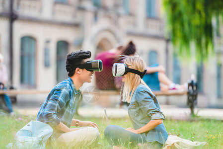 虚拟现实头戴着坐在公园绿草地上的虚拟真人耳机中多文化学图片
